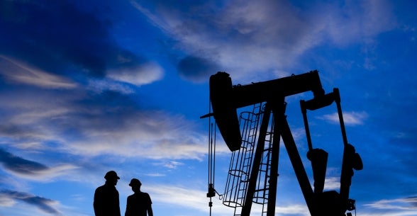 Sunset silhouette of an oil rig and two workers standing nearby