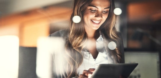 Image of a woman in a suit smiling at a tablet.