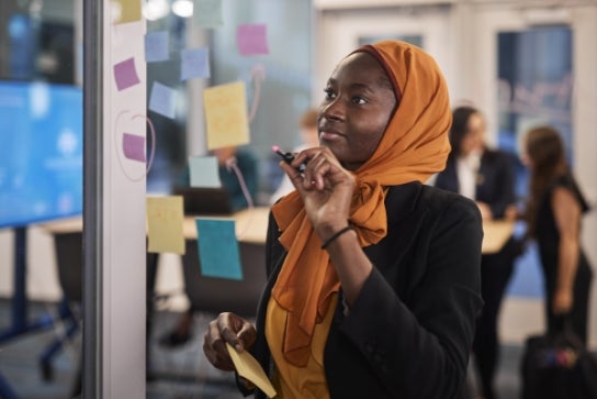 Image of a Thunderbird student writing on a board with post it notes during a meeting