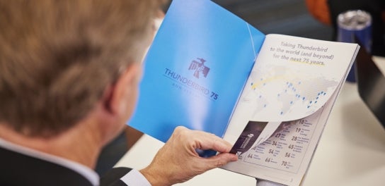 Image of a Thunderbird Alumnus flipping through a Thunderbird magazine