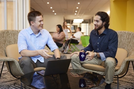 Two Thunderbird students chat in front of a laptop.