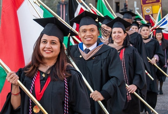Image of Thunderbird graduates in full regalia marching in the flag procession